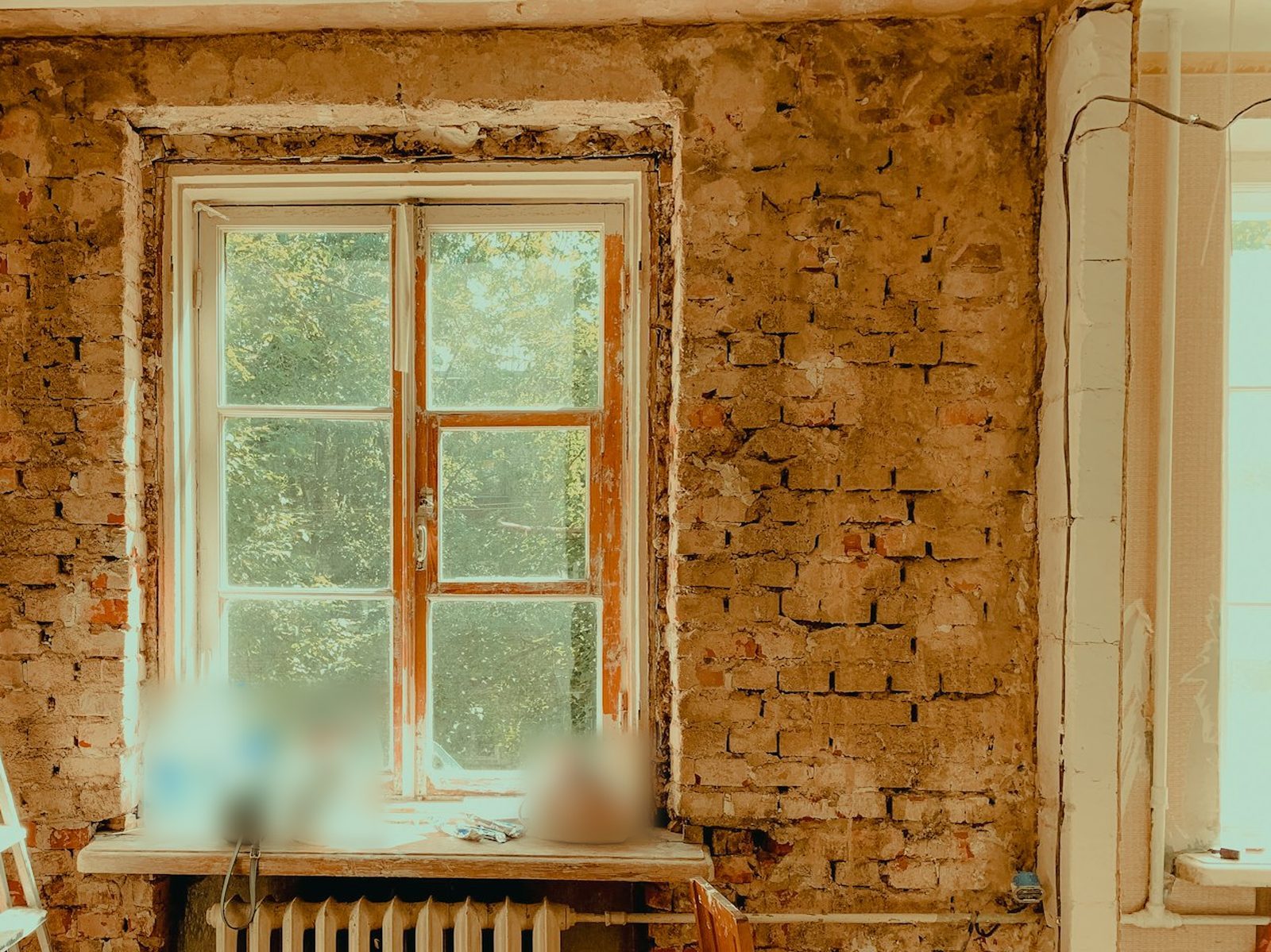 Moderne Website für einen Sanierungsbetrieb, Beispielansicht: Altbauzimmer im Rohzustand: freigelegtes Ziegelmauerwerk, altes Holzfenster mit Blick ins Grüne, darunter ein Heizkörper und eine Leiter